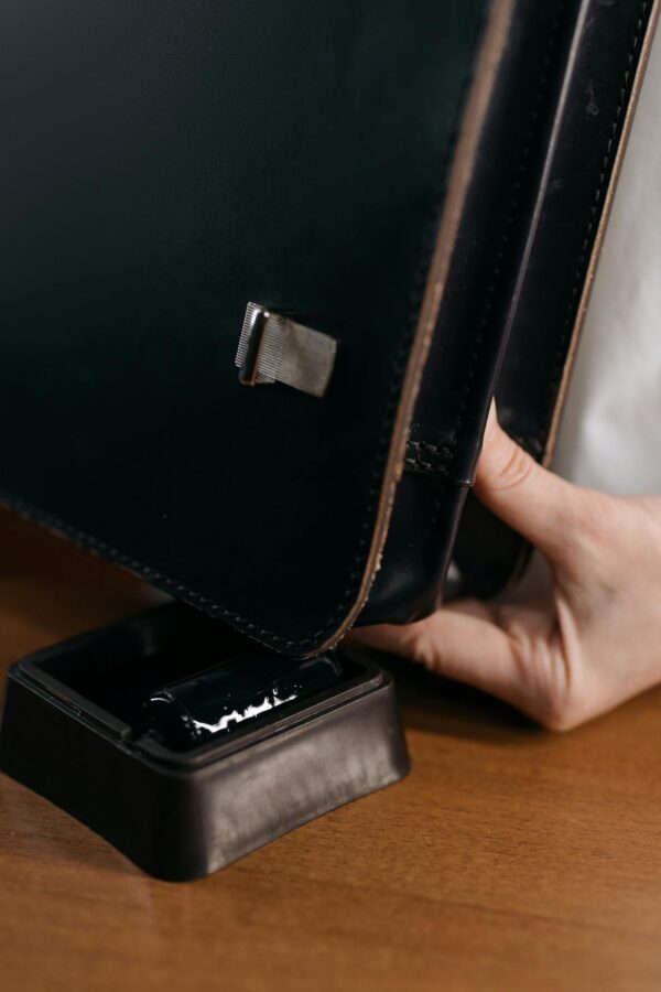Detailed view of a person holding a black leather bag on a wooden surface, featuring elegant design.
